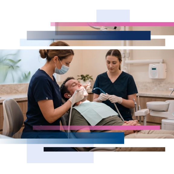 Dentist and assistant performing dental treatment on male patient in a clinic setting.