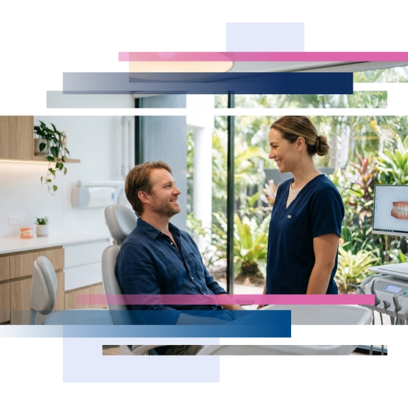 Dentist consulting with a male patient seated in a dental chair in a modern clinic with greenery visible outside.