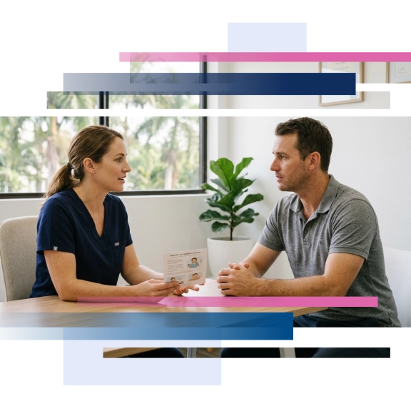 Dentist discussing treatment with a male patient at a consultation table, with a plant and window in the background.