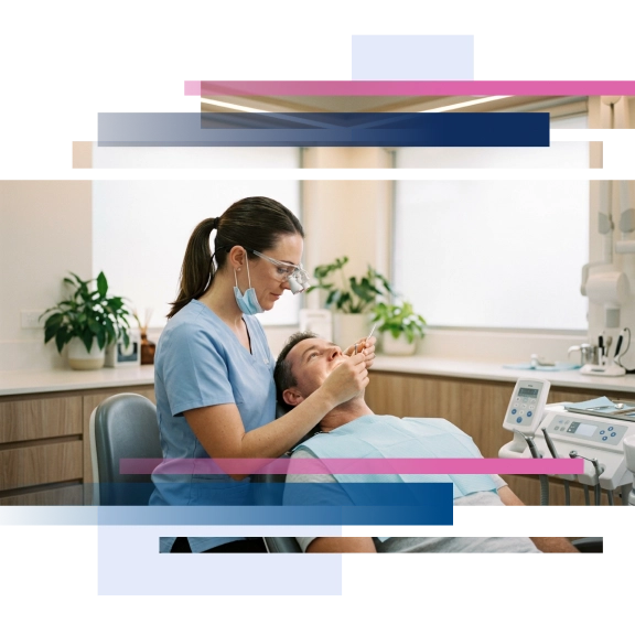 Dentist examining patient's mouth in dental chair, both wearing masks, in a bright dental office setting.
