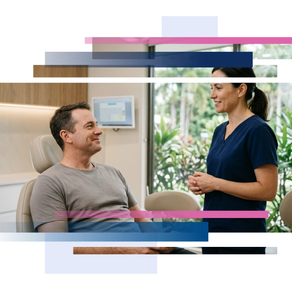 Patient sitting in a dental chair smiling at a dentist who is speaking, with greenery visible outside the window.