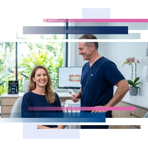 Smiling woman seated in a dental office while a man in scrubs stands beside her.